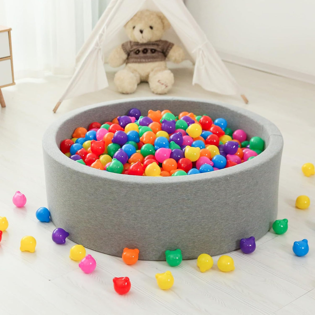 Multicolour bear-shaped plastic balls arranged in a grey ball pit inside a bright playroom.