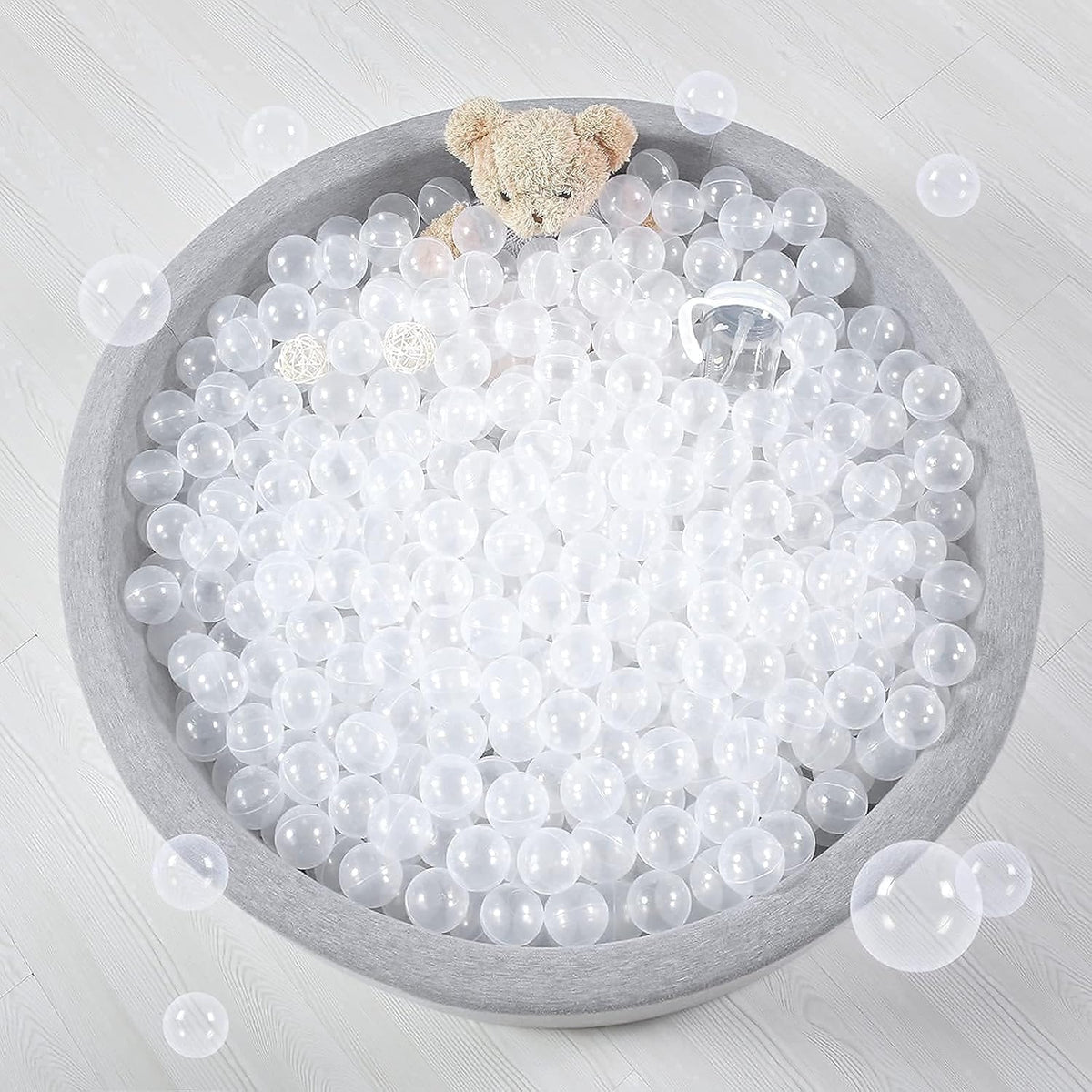 Grey fabric ball pit filled with clear transparent plastic balls and a teddy bear.
