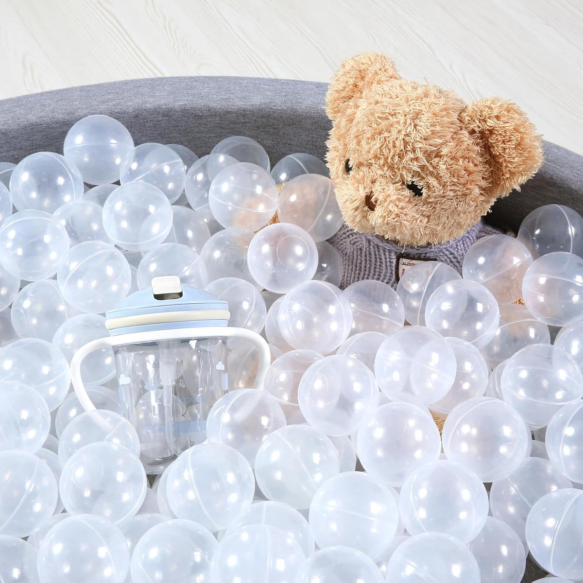 Clear transparent ball pit balls arranged around a teddy bear and children’s drinking cup.